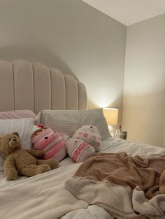 two teddy bears laying on a bed with pillows and blankets in the foreground, next to a lamp