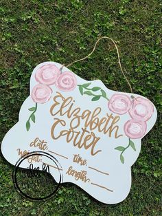 a white sign with pink flowers on it sitting in the grass next to a pair of scissors