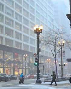 people are walking in the snow on a city street with traffic lights and buildings behind them