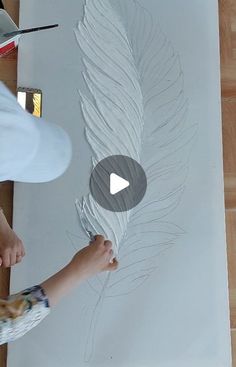 a person is drawing on a piece of paper with white paint and a brush in front of them