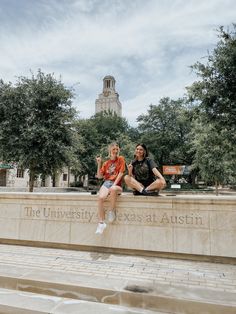 two people are sitting on a wall in front of the university of texas at austin