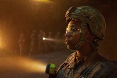 a soldier wearing goggles and holding a flashlight in his hand while standing on a dirt road at night