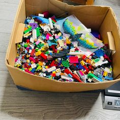 a cardboard box filled with legos on top of a wooden floor next to a digital clock