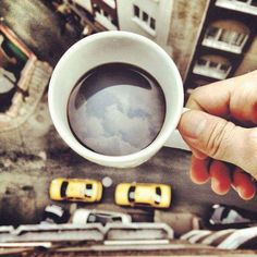 a person holding a coffee cup in front of a building and taxi cabs on the street