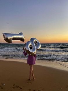 a woman standing on top of a sandy beach holding up two large air filled balloons