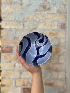 a hand holding a blue and white bowl in front of a brick wall with shelves