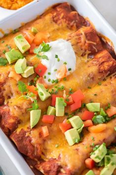 an enchilada casserole in a white dish with sour cream on top