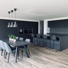 a dining room table surrounded by chairs in front of a kitchen with black cabinets and an island