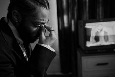 a black and white photo of a man in front of a tv holding his hand to his face