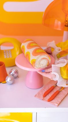 an assortment of colorful objects on a pink and yellow tablecloth, with a phone in the background