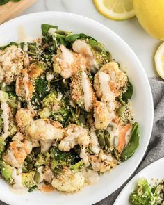 a white bowl filled with broccoli and cauliflower next to lemon wedges