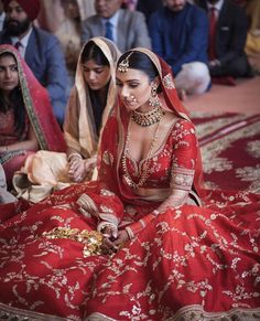 a woman in a red and gold bridal dress sitting on the floor with other people