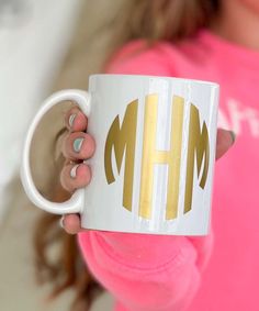 a woman holding a coffee mug with the letter h in gold and white on it