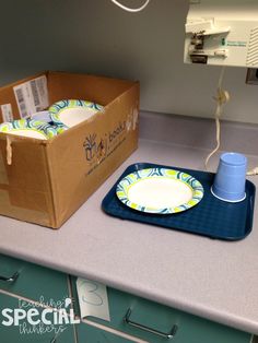 a box with two plates on it next to a blue cup and an electrical outlet