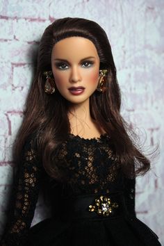 a doll with long brown hair wearing a black dress and gold earrings on her head