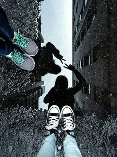 two people standing in front of a puddle with their feet on the ground and one person's reflection