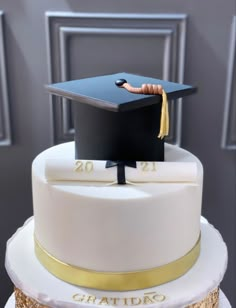 a white and gold graduation cake with a black cap on top