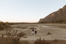 two people are walking in the sand near water