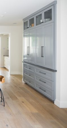 an empty kitchen with gray cabinets and wood flooring, along with a bar stool