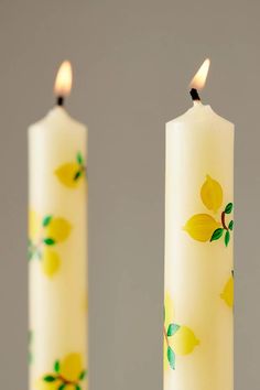 two candles with yellow flowers painted on them, one lit and the other turned off