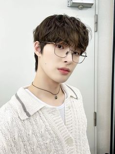 a young man with glasses and a white sweater is standing in front of a mirror