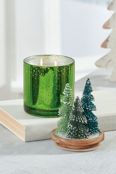 a green candle sitting on top of a table next to a small tree and book