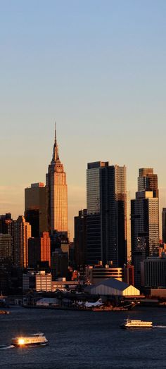 the city skyline is lit up at sunset with boats in the water and one plane flying overhead