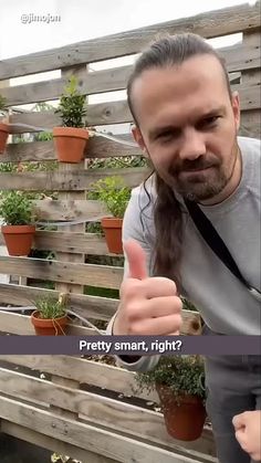 a man giving the thumbs up sign with potted plants in the back ground behind him