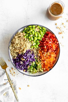 a bowl filled with different types of food next to a fork and spoon on a white surface