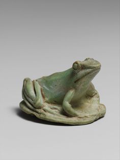 a green frog sitting on top of a piece of pottery with its eyes closed and it's legs crossed