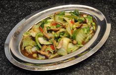 a silver plate filled with vegetables and meat on top of a table next to a black counter