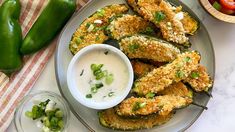 a plate full of fried zucchini and dip next to some green peppers on the side