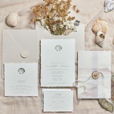 the wedding stationery is laid out on top of the table with shells and seashells