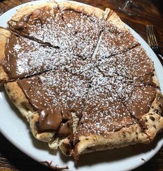 a chocolate pie with powdered sugar on top sits on a white plate next to a fork