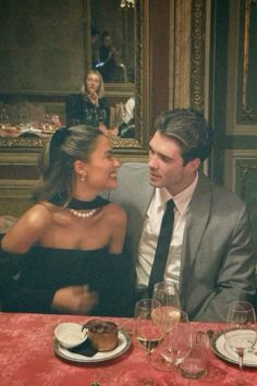 a man and woman sitting at a table in front of each other with wine glasses