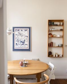 a wooden table with two white chairs in front of it and a shelf on the wall