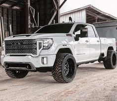 a white truck parked in front of a building with large tires on it's tires