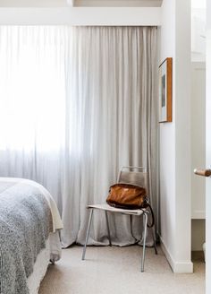 a bed room with a neatly made bed next to a window and a bag on a chair