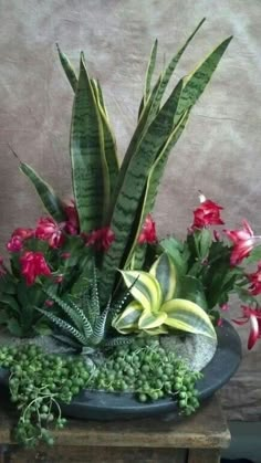 an arrangement of flowers and greenery in a bowl on top of a wooden table