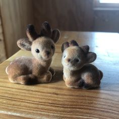 two small stuffed animals sitting on top of a wooden table next to each other and looking at the camera