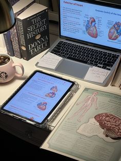 an open laptop computer sitting on top of a desk next to a book and cup