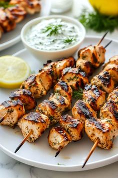 grilled chicken skewers on a white plate with lemon wedges and dip