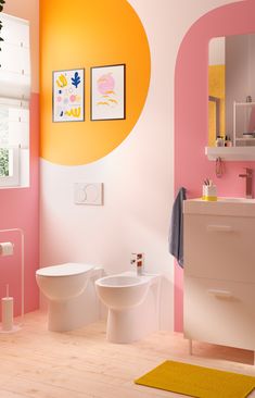 a bathroom with pink and yellow walls, two toilets and a white sink in the corner