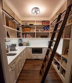 a ladder is in the middle of a kitchen with white cabinets and wood flooring