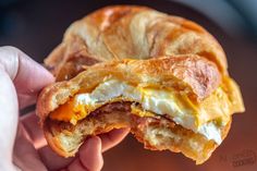 a hand holding a pastry with an egg and cheese filling in it's center