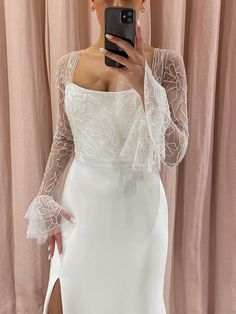 a woman taking a selfie in front of a mirror wearing a white dress with sheer sleeves