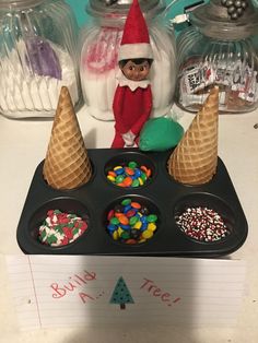 an elf is sitting on top of a muffin tray with candy and sprinkles