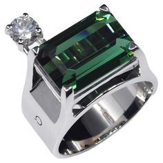 a ring with an emerald colored stone and two diamonds on the top, set in white gold