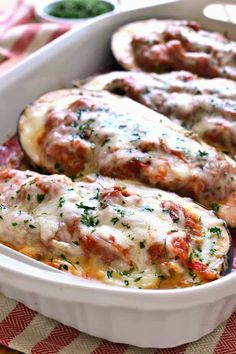 an oval casserole dish filled with meat covered in sauce and cheese, on a red checkered tablecloth