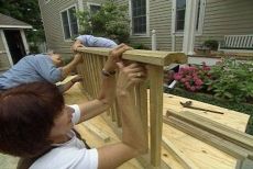 two people are building a wooden fence on a deck in front of a house and one person is holding the railing